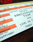 Ticket-style invitation for an 'Anniversary Tour' with decorative elements on a wooden surface.