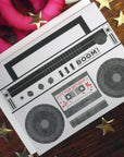 Greeting card with a retro boombox design on a wooden surface with decorative stars.