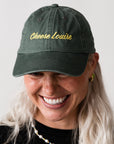 Person wearing a green cap with 'Cheese Louise' embroidered on it against a plain background