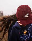 Person wearing a maroon cap with a bird design, covering their face, against a blurred background.