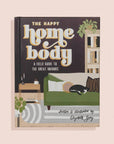 Book cover of 'The Happy Home Body' with a living room illustration on a beige background