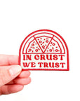 Patch with 'In Crust We Trust' text held by a hand on a white background