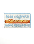 Embroidered patch with a baguette and text 'less regrets more baguettes' on a white background