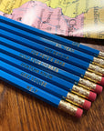 Blue pencils with humorous text on erasers on a wooden surface with a map in the background
