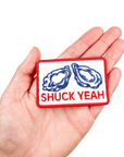 Patch with oyster design and 'SHUCK YEAH' text held in a hand on a white background