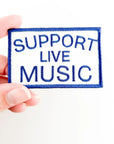 Patch with 'Support Live Music' text held by a hand on a white background