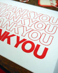 White card with red 'THANK YOU' text on a wooden surface