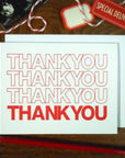 White card with 'THANK YOU' text repeated in red, on a wooden surface with a pencil and decorative elements.