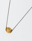Simple brass U shape with a circular disk threaded onto a silver chain. The necklace is 18 inches long with a clasp.