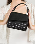 Black handbag with eye pattern held by a person against a light background