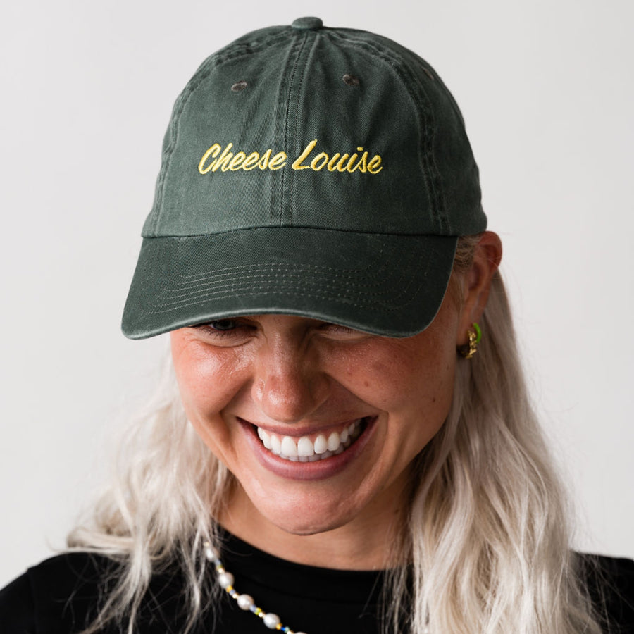 Person wearing a green cap with 'Cheese Louise' embroidered on it against a plain background