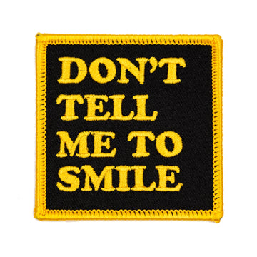 Patch with 'DON'T TELL ME TO SMILE' text in yellow on a black background