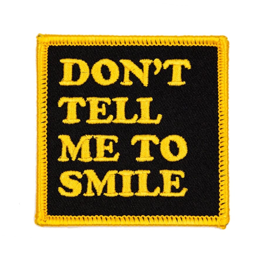 Patch with 'DON'T TELL ME TO SMILE' text in yellow on a black background