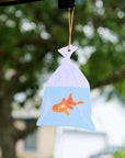 Decorative car hanging with a fish design against a blurred outdoor background