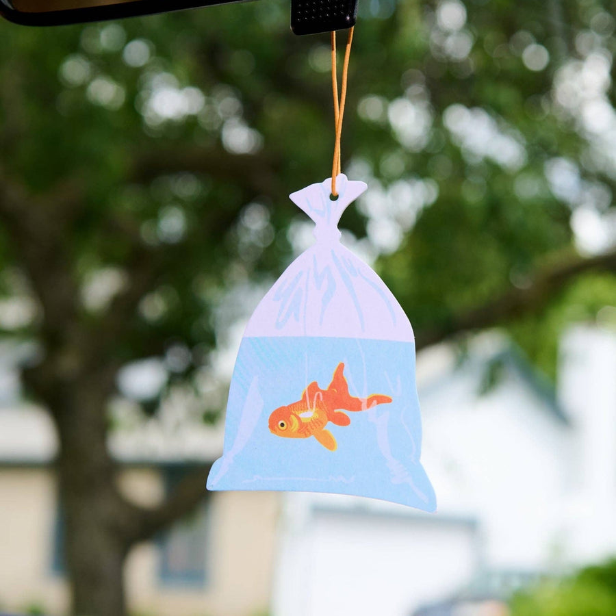 Decorative car hanging with a fish design against a blurred outdoor background