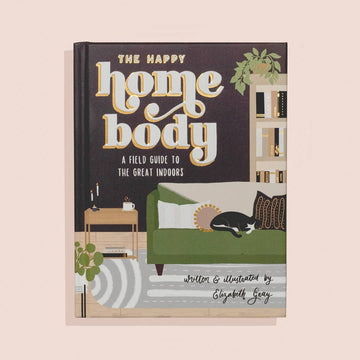Book cover of 'The Happy Home Body' with a living room illustration on a beige background