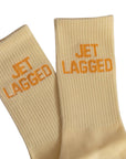 Beige socks with 'JET LAGGED' text in orange on a white background