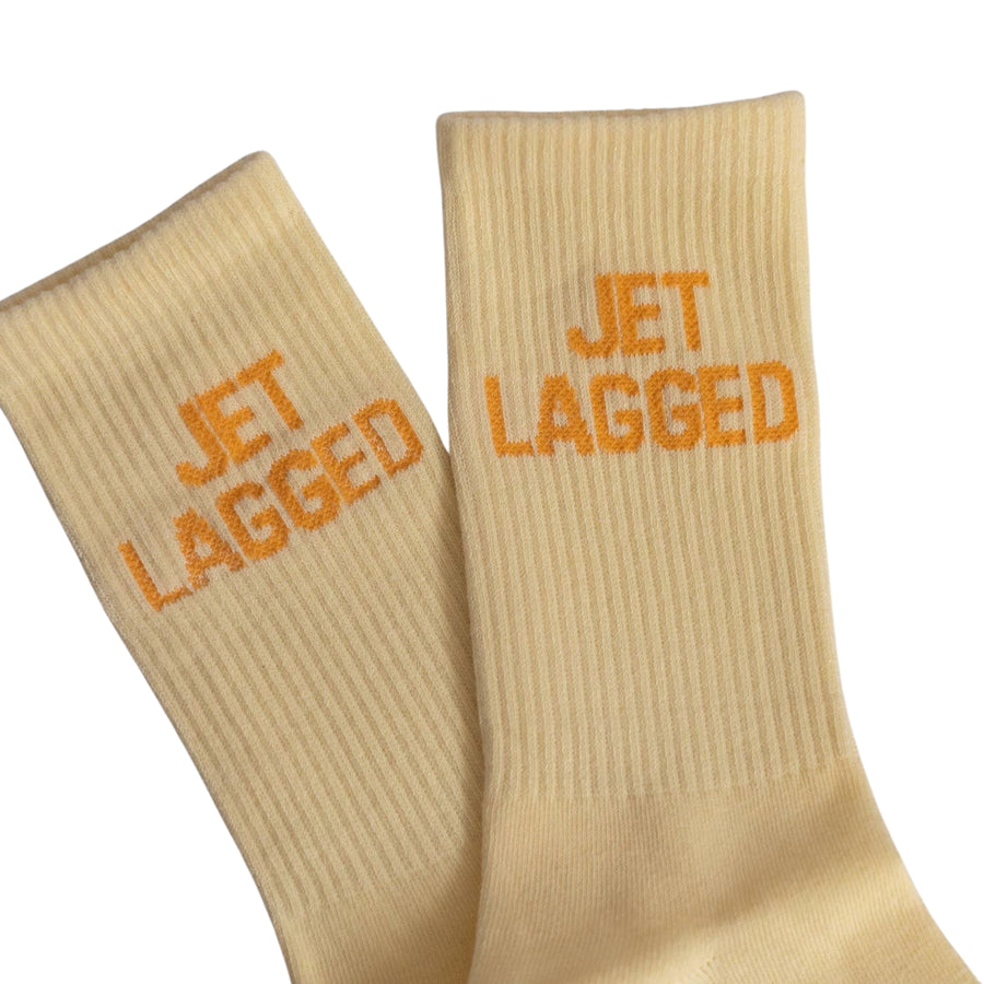 Beige socks with 'JET LAGGED' text in orange on a white background
