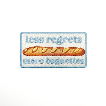 Embroidered patch with a baguette and text 'less regrets more baguettes' on a white background