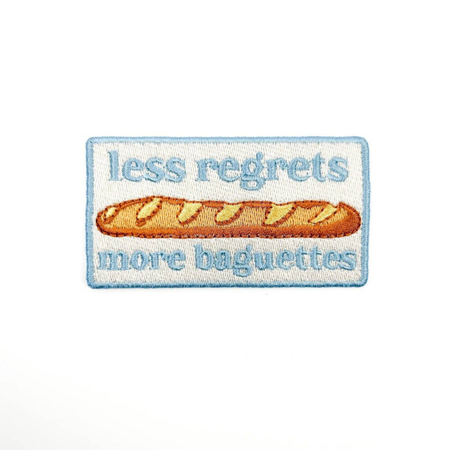 Embroidered patch with a baguette and text 'less regrets more baguettes' on a white background