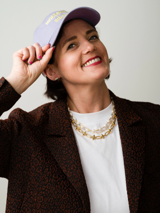 Woman wearing a cap and smiling against a plain background