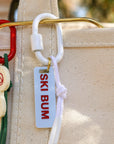 Keychain with 'Ski Bum' tag attached to a beige bag