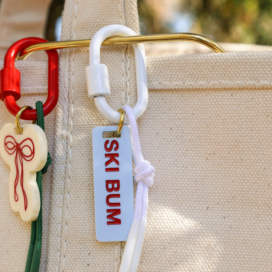 Keychain with 'Ski Bum' tag attached to a beige bag