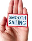 Hand holding a patch with 'Smooth Sailing' text on a white background
