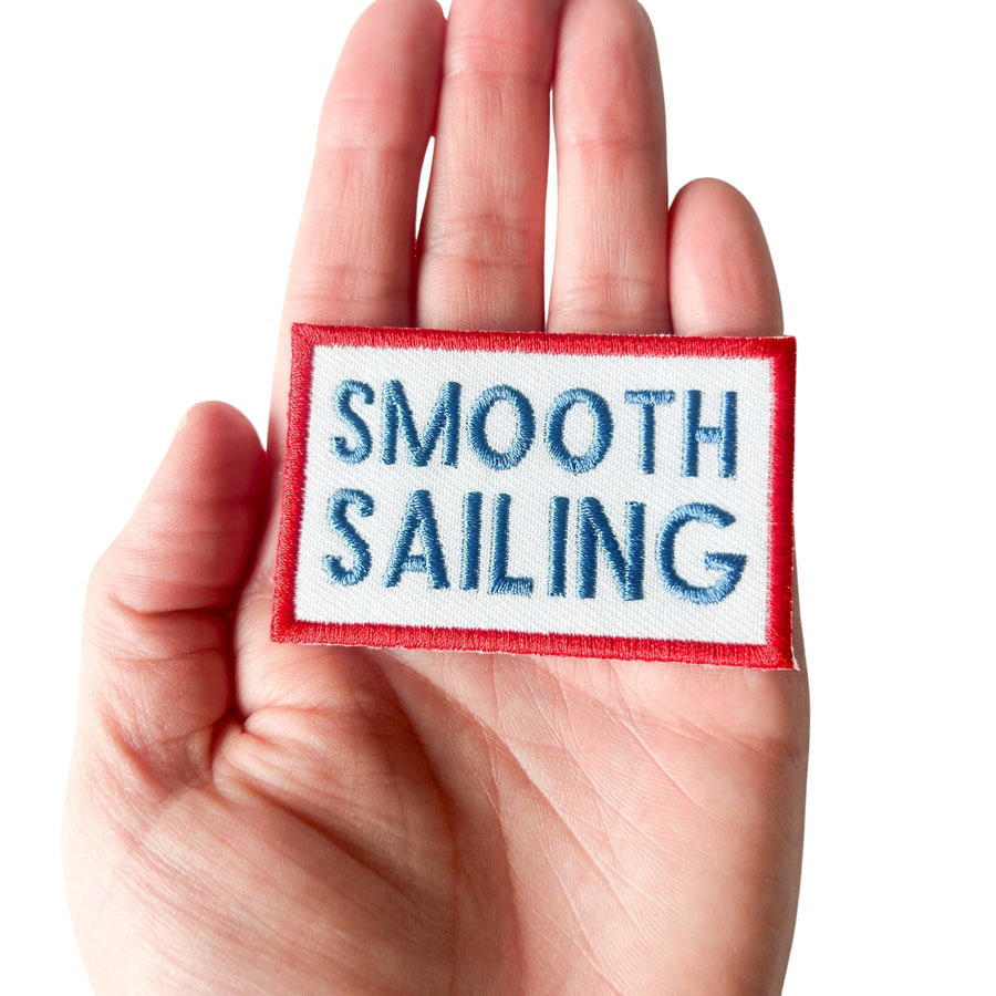 Hand holding a patch with 'Smooth Sailing' text on a white background