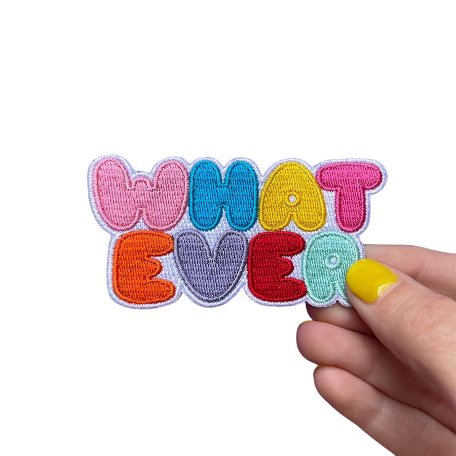 Colorful patch with 'WHAT EVER' text held by a hand on a white background