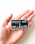 Hand holding a patch with 'Whiskey Bent & Hellbound' text against a white background
