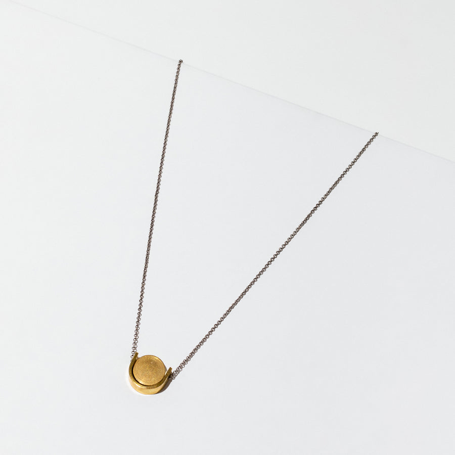 Simple brass U shape with a circular disk threaded onto a silver chain. The necklace is 18 inches long with a clasp.